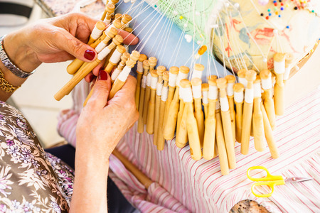 Unrecognizable senior woman with red nails weaving with bobbins and threads in close-upの写真素材