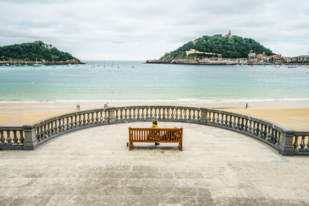 SAN SEBASTIAN,SPAIN - 30 AUGUST,2016: Back view of three adult tourists sitting on bench at viewpoint and watching seascape of San Sebastian Concha beach.のeditorial素材