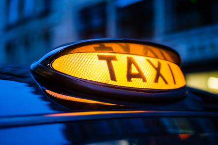 An illuminated with yellow taxi sign on a car roof at night. の写真素材