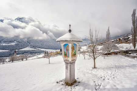 View on religious stone post with paintings and cross in winterlandの写真素材