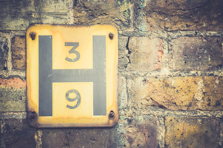 A plate with H letter and three and nine numerals hanging on a brick wall.の写真素材