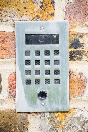 A metal doorbell with the camera hanging on a brick wall.