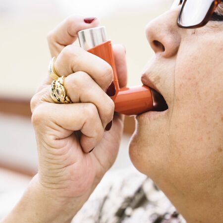 Side view of senior woman in glasses using inhalerの写真素材