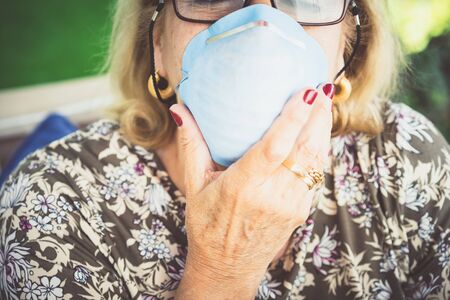 Close-up of senior blonde woman in glasses wearing inhaling maskの写真素材