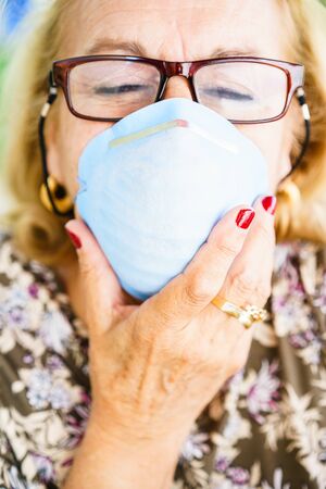 Close-up of senior blonde woman in glasses wearing inhaling maskの写真素材