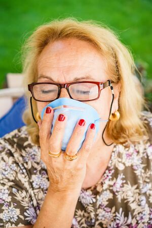 Close-up of senior blonde woman in glasses wearing inhaling maskの写真素材