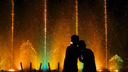 Two kids watching fountain in the colorful night scene.の写真素材