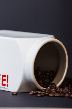 Black coffee beans pouring from a white ceramic jarの写真素材