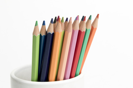 A group of multi colored pencils in a white cup on an isolated backgroundの写真素材