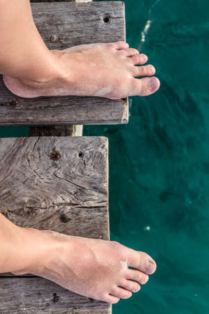 Bare feet standing by the ocean on a wooden pier POV shotの写真素材