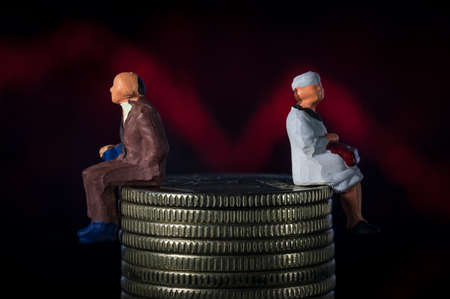 Miniature people. Senior old couple sitting on stack of coins. Red line plunge chart background....