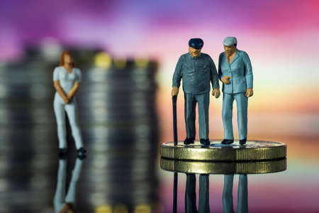 Miniature people old couple walking with a cane nurse in the background. Concept of retirement...