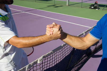 Two men, professional tennis players shake hands before and after the tennis match. In the photo it looks like shaking hands greeting each other closely.の写真素材