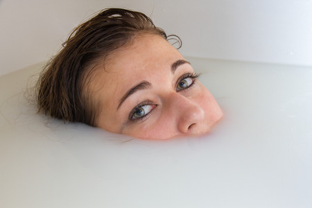 Blue-eyed blonde girl bathing in a bathtub full of milk and water. The photo is a portrait of His...