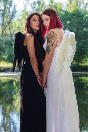 Two white girls dressed in black and white angels with wings on His back standing on a pier on a lake in the Finnish forest in Madrid, Spain.の写真素材