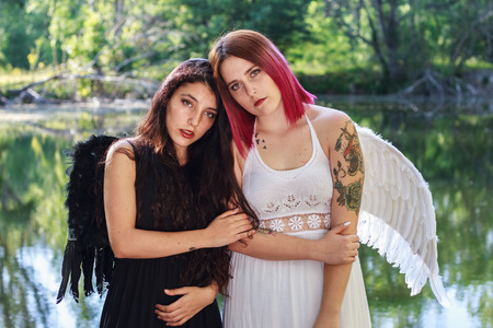 Two white girls dressed in black and white angels with wings on His back standing on a pier on a lake in the Finnish forest in Madrid, Spain.の写真素材