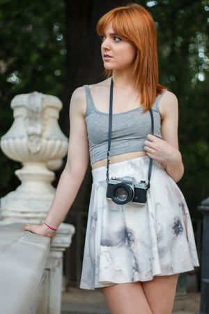 Young girl with orange hair taking pictures With an old camera retro style in a city park. She is happy to be reliable to use a camera reel again.の写真素材
