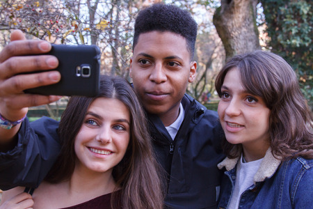 Group of young people, two girls and a black caucasian boy doing a selfie in the field with a cell phone. They are friends.の写真素材