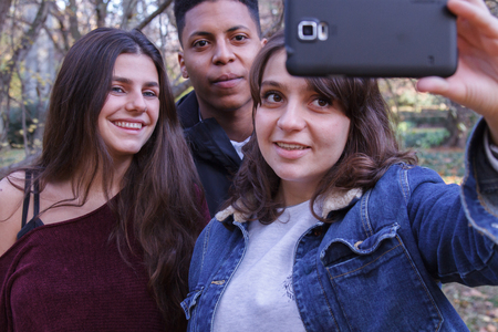 Young people of different races taking a selfie With the smartphone in the park. They are friends and enjoy a nice day outdoors.の写真素材