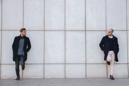 Two young entrepreneurs dressed in modern and elegant clothes leaning against a white wall. They are business partners - business, modern, hipster, success conceptの写真素材