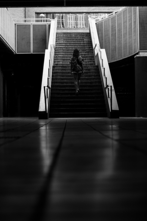 Black and white photograph of a black silhouette of a girl walking towards a few stairs in the city.の写真素材