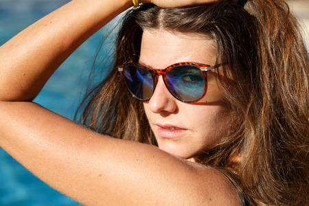 Portrait of beautiful brunette wearing sunglasses and posing in pool looking at camera.