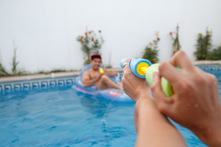 Young friends shooting with water guns at each other while having fun in pool.の写真素材