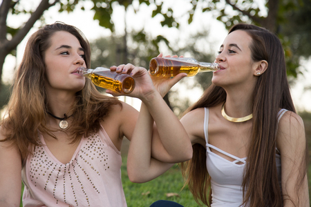 Two young stylish women relaxing together in park and drinking beer looking at each other.の写真素材