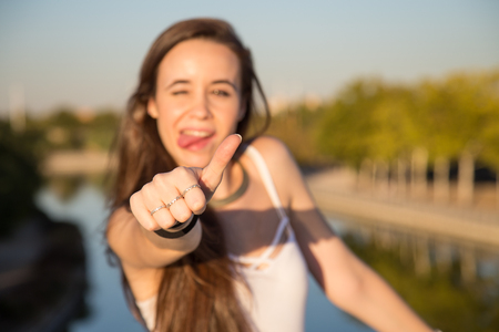 Happy-looking young woman standing in park on sunny day and gesturing thumb up.の写真素材