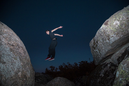 From below view of sportive man jumping from rock to rock doing parkour in dark night.