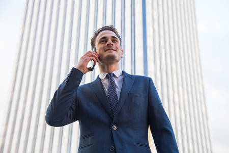 Cheerful stylish businessman wearing formal suit and having phone talk posing on urban background.の写真素材