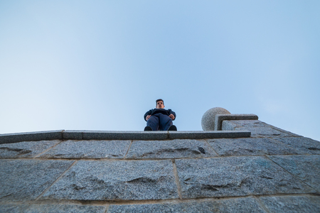 Young man standing on top of a wall leaning out to look at the ground while doing parkour.