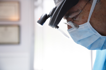 Side view of serious professional dentist wearing glasses and working with concentration in clinic.の写真素材