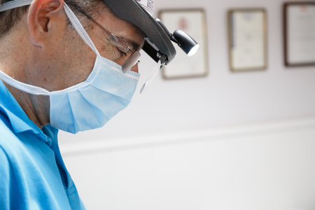 Side view of serious professional dentist wearing glasses and working with concentration in clinic.