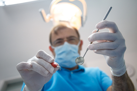 From below shot of dentist in uniform and gloves using tools and doing oral cavity inspection in dental cabinet.の写真素材