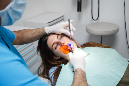 Crop view of hands of dentist in gloves doing tooth filling to young female.の写真素材