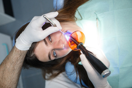 Crop view of hands of dentist in gloves doing tooth filling to young female.の写真素材