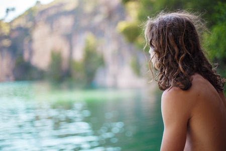 Young man looking at the greenish lake in the mountains at sunny day seen from his back.の写真素材