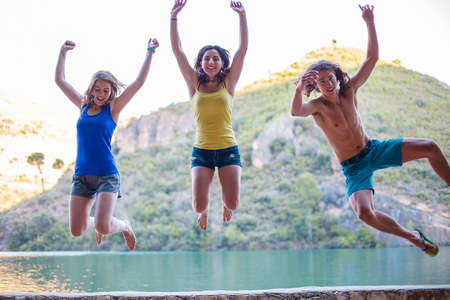 Friends jumping on a embankment on a turquoise lake in the mountainsの写真素材