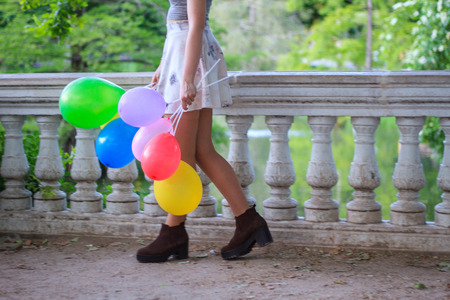 Young woman with colorful balloons in a greenish park on sunny day in a celebration.の写真素材
