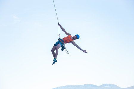 View of man in hardhat hanging on rope while doing rappel and showing pirouettes flying in air