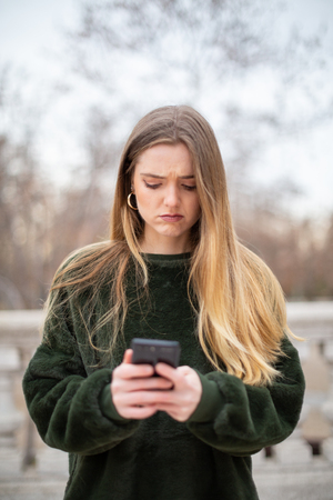 Worried woman looking at smartphone in parkの写真素材