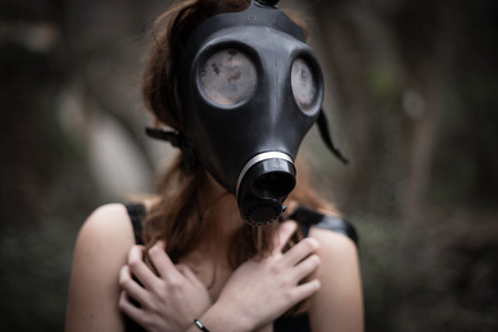 Portrait of anonymous woman in black clothes and gas mask standing in amazing spooky forestの写真素材
