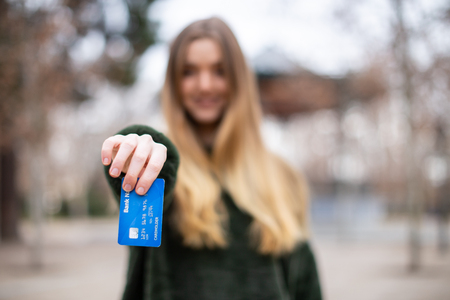 Happy young lady with credit card while standing in parkの写真素材