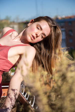 Portrait of young attractive woman in casual summer dress leaning on railing of balconyの写真素材