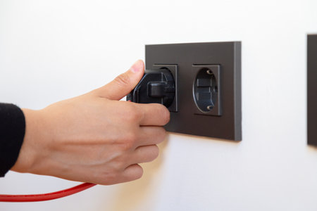 Closeup of male hand plugging electrical outlet on white wall.