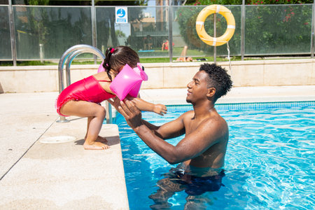 African american father and daughter playing in swimming pool on a sunny day