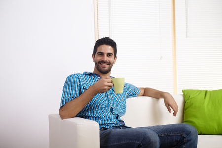 Young man drinking coffee in a couch.の写真素材