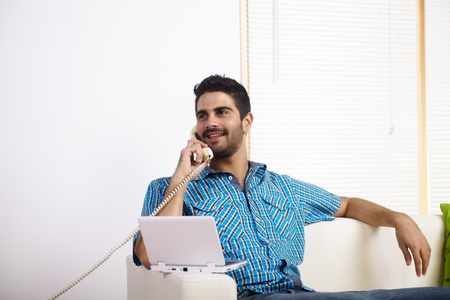 Young man using a laptop while on the phone.の写真素材