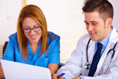 Portrait of a young doctor and a nurse talking and using a laptop on the office.の写真素材